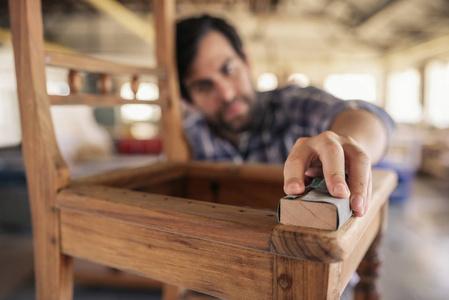 一家家具制造商在木工车间工作时用砂纸打磨一把木椅照片